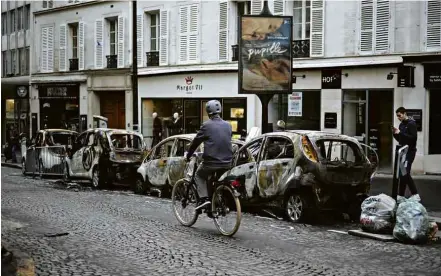  ??  ?? Ciclista passa em rua de Paris neste domingo ao lado de carros queimados em protesto no sábado