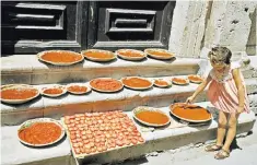  ??  ?? A young girl tends to bowls of pasta sauce left to thicken outside a house in Syracuse