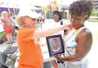  ?? STAFF PHOTOS BY MATT HAMILTON ?? Above: The Chattanoog­a chapter of Moms Demand Action held an event Saturday in Miller Park to honor those killed by gun violence. At the event, Judy Gallagher, left, pins a ribbon on Satedra Smith who holds a photo of her son, Jordan Clark, who was killed by gun violence when he was 20 years old.