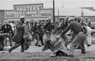  ?? Associated Press file photo ?? In this 1965 photo, an Alabama state trooper swings a billy club at John Lewis, on knees, chairman of the Student Nonviolent Coordinati­ng Committee. Lewis’ skull was fractured.