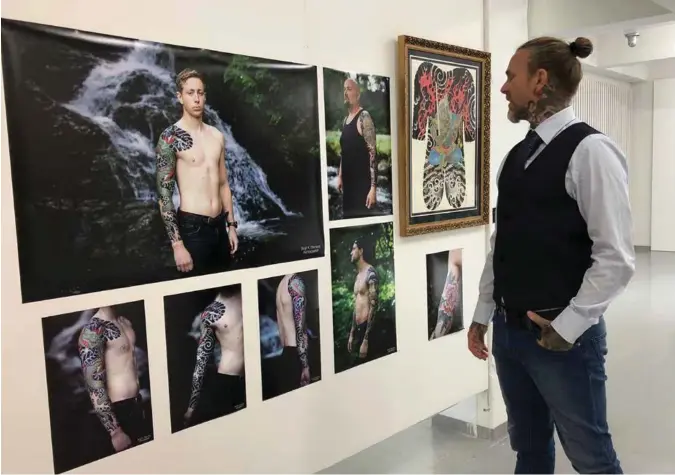  ??  ?? Glenn Flesjaa foran bildene av sine egne tatovering­sverk og maleriet av en body suit.