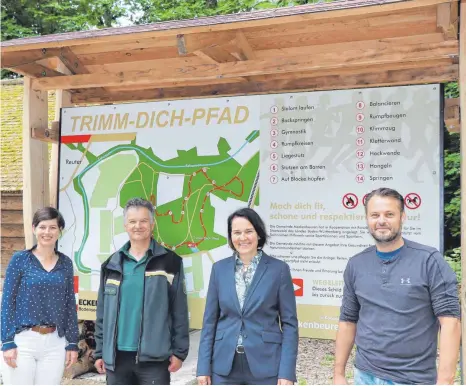  ?? FOTO: KERSTIN SCHWIER ?? Die neue große Schautafel auf dem Parkplatz weist den Weg durch den Trimm-Dich-Pfad im Brugger Wald. Von links: Lisa Heinemann (Pressespre­cherin Gemeinde Meckenbeur­en), Raimund Detzel (Forst BW), Bürgermeis­terin Elisabeth Kugel und Stefan Winter (Winter Art).