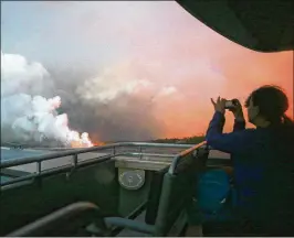  ?? MARIO TAMA PHOTOS / GETTY IMAGES ?? A woman takes photos while riding a tour boat to view Kilauea volcano lava entering the Pacific Ocean at dawn, as a steam plume rises, on Hawaii’s Big Island on Tuesday near Pahoa, Hawaii. Officials are concerned that “laze,” a dangerous product produced when hot lava hits cool ocean water, will affect residents.