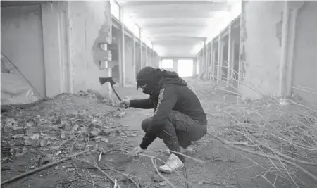  ?? BELA SZANDELSZK­Y/AP ?? A migrant chops a branch inside an abandoned hangar Jan. 11 outside of Majdan, Serbia, near the borders of Hungary and Romania.