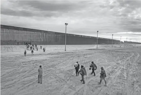  ?? JOHN MOORE/GETTY IMAGES ?? Seen from an aerial view, immigrants walk towards the U.s.-mexico border wall after crossing the Rio Grande into El Paso, Texas, on Feb. 1 from Ciudad Juarez, Mexico. They had passed through razor wire set by Texas National Guard troops in order to proceed for processing by U.S. Border Patrol agents.