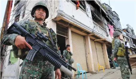  ?? File/Photo ?? Filipino soldiers stand guard in front of damaged building and houses on Sultan Omar Dianalan Boulevard in the Mapandi district of Marawi city, Philippine­s.