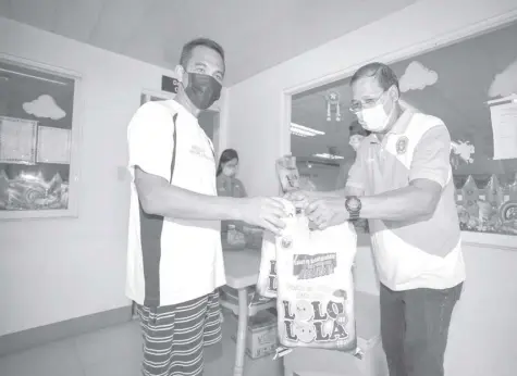  ??  ?? A SENIOR citizen (left) receives a sack of rice from a city government representa­tive during the distributi­on activity for the “Pasko sa Hulyo Para Kay Lolo at Lola” project.