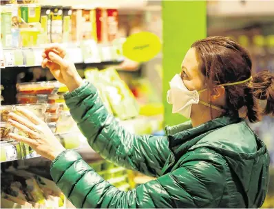  ??  ?? Precaution: A shopper scans a supermarke­t shelf while wearing a mask. Figures show supermarke­ts do not appear to be breeding grounds for the virus