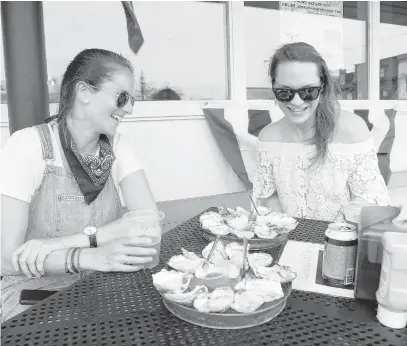  ?? PAUL W. GILLESPIE/CAPITAL GAZETTE ?? Valerie Parra, left, and Brianna Garrold eat oysters and drink beer outside the Market House after Annapolis and Anne Arundel County bars and restaurant­s were allowed to open to outdoor dining starting at 5 p.m. Friday.