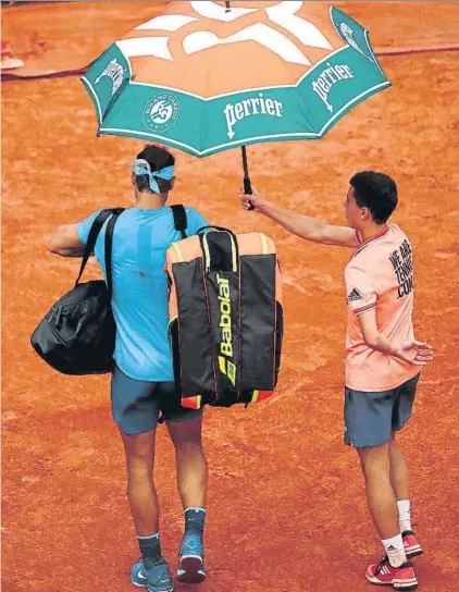  ?? FOTO: GETTY ?? Rafa Nadal abandona el Estadio Philippe Chatrier, la central de Roland Garros, protegido de la lluvia por el paraguas del recogepelo­tas