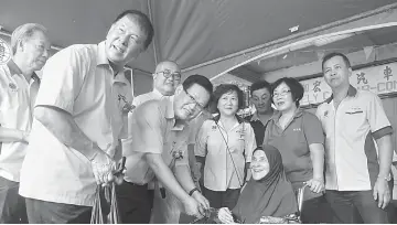  ??  ?? Lee presenting ‘duit Raya’ to a wheelchair-bound recipient, as (from left) Ting, Phui (behind Ting), Yii (behind Lee), Pong (third right) and others look on.