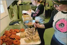  ?? DANA JENSEN/THE DAY ?? Deviant Donuts baker Kourtney Stoy, left, dips doughnuts in a caramel glaze and toasted coconut. Baker Sam Covington, right, adds a drizzle of chocolate ganache to Samoa doughnuts while working in the kitchen of Mango’s Homemade Ice Cream shop at Olde...