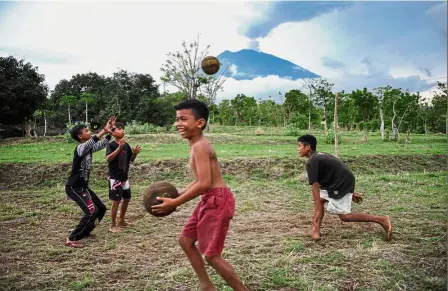  ??  ?? Imminent threat: Children playing as Mount Agung looms in the distance in Karangasem. — AFP