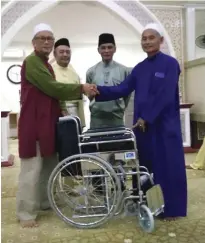  ??  ?? Hanapi (left) presents the wheelchair to Mohamad Cek.