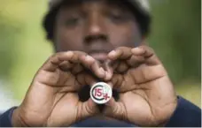  ?? GRAHAM HUGHES/THE CANADIAN PRESS ?? Montreal Old Port worker Konrad Lamour holds up a badge illustrati­ng a demand for a minimum hourly wage of $15.