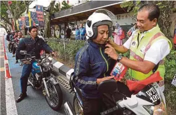  ??  ?? AB Aziz memakaikan topi keledar kepada penunggang motosikal di Menara 1 DBKL, semalam.