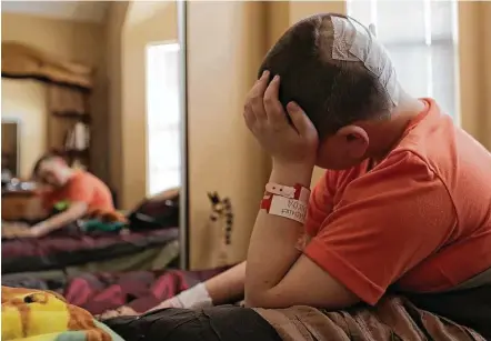  ?? Elizabeth Conley / Houston Chronicle ?? Brayden sits up on his bed in his family’s condo rental near the Texas Medical Center after being released from the hospital. Within a day of surgery he was up and walking, and within a week he told doctors that the pain in his head had all but faded.