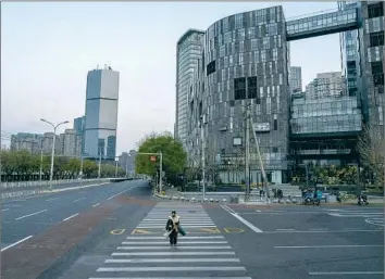  ?? Kevin Frayer Getty Images ?? A WOMAN crosses a road during rush hour in Beijing’s central business district on Nov. 22. In an effort to rein in COVID-19 outbreaks, offices had to close down and people were expected to work from home.