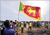  ?? PTI ?? A Sri Lankan man holds a national flag as police officers conduct investigat­ions into aftermath of clashes between government supporters and anti government protesters in Colombo, Sri Lanka, Tuesday