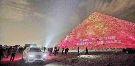  ?? — AFP photo ?? People take pictures in front of the Great pyramid of Kheops where a laser projection writes ‘Stay at home, stay safe. Thanks to those keeping us safe’ amid the spread of the Covid-19 infection, caused by the novel coronaviru­s.