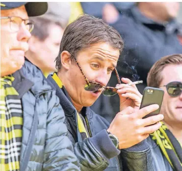 ?? FOTO: IMAGO ?? Ein Fan von Borussia Dortmund rückt sich beim Spiel gegen Hertha BSC sich seine Brille von den Augen, um auf seinem Smartphone besser sehen zu können.