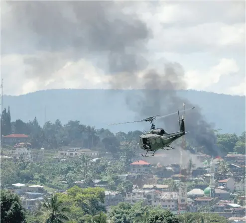  ?? NOEL CELIS / AFP / GETTY IMAGES FILES ?? A helicopter flies through smoke billowing from houses after airstrikes by Philippine air force planes on Islamist militant positions in Marawi on the southern island of Mindanao on June 17.