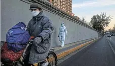  ?? /Getty Images /Kevin Frayer ?? Gradual reopening: A cyclist rides past an epidemic control worker in Beijing on Sunday.