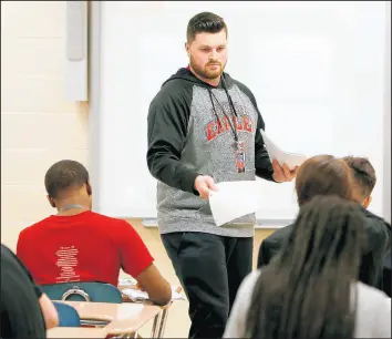  ?? SUZANNE TENNANT/POST-TRIBUNE ?? Health/physical education instructor Justin Fidnarik hands out paper to his high school class at Lake Station Edison High on Wednesday.