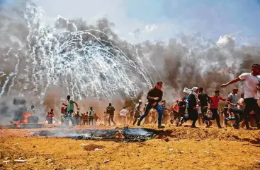  ?? Mohammed Abed / AFP / Getty Images ?? Palestinia­ns run for cover from tear gas Monday as Israeli forces opened fire near the border between Israel and the Gaza Strip. The protests began weeks ago over an economic blockade.