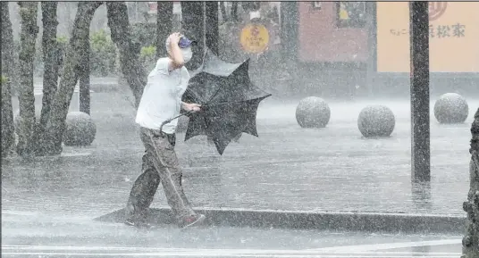  ?? The Associated Press ?? A man gets drenched Saturday on Japan’s main Honshu island as umbrellas were no match for Tropical Storm Meari’s heavy rain and swirling winds. The storm was headed toward Tokyo, according to Japanese weather officials.