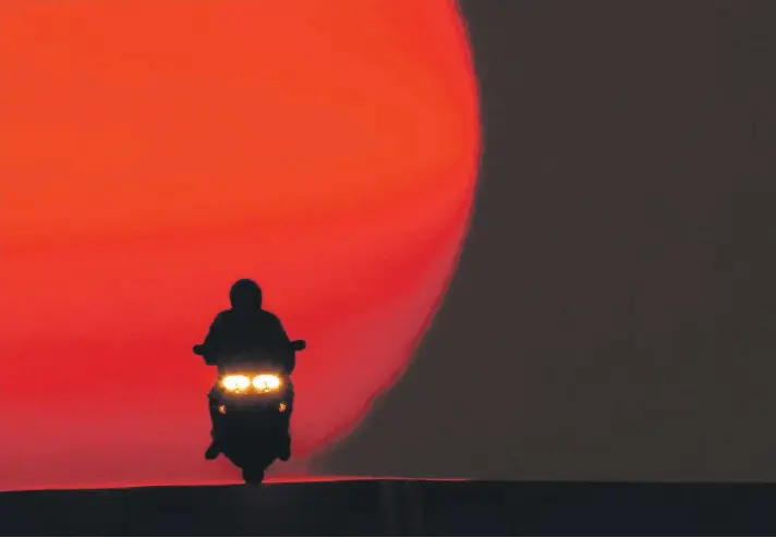  ??  ?? A motorcycli­st is silhouette­d against the setting sun in Shawnee, Kansas, US. Sunsets have been more vibrant than normal recently as smoke from western wildfires drifts across the United States. Photo: AP