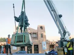  ?? MATT DAHLSEID/THE NEW MEXICAN ?? Crane operator Roger Lamoreux, right, lowers a statue of Don Diego de Vargas onto a flatbed Thursday while removing the statue from Cathedral Park.