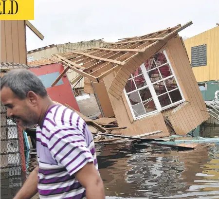  ?? HECTOR RETAMAL / AFP / GETTY IMAGES ?? A man walks past a house laying in flood water in Catano, Puerto Rico, after the U.S. territory was battered by hurricane Maria. Communitie­s across Puerto Rico remained isolated and without communicat­ion as uprooted trees blocked roads and people...