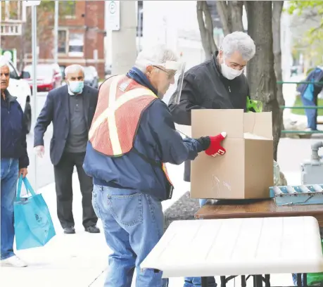  ?? NICK BRANCACCIO ?? Volunteer Marcel Hinse, centre, assists food basket recipients at the Windsor Goodfellow­s on Park Street West on Tuesday.