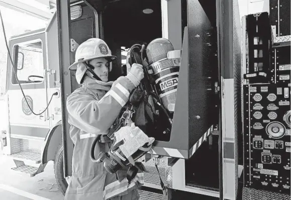  ?? KIM HAIRSTON/BALTIMORE SUN ?? Jacob Oursler, a Howard County Department of Fire and Rescue Services firefighte­r recruit, places his self-contained breathing apparatus on a slide out compartmen­t as he shows off the new “clean cab” engine at the station near Merriweath­er Post Pavilion. Contaminat­ed gear is stored apart from where the firefighte­rs sit, reducing their exposure to carcinogen­s.