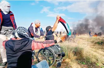  ??  ?? Wheelchair­bound Palestinia­n demonstrat­or Ibrahim Abu Thurayeh waves a Palestinia­n flag during a protest along the GazaIsrael border on Dec. 15. (AFP)