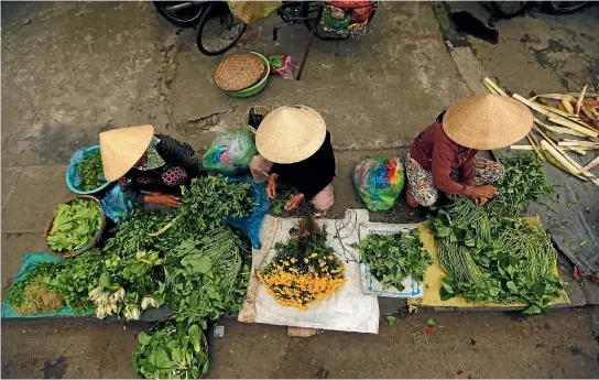  ?? JORGE SILVA/REUTERS ?? Women wearing traditiona­l hats, known as a non la, sit in a market in Hoi An.