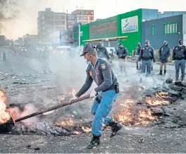  ?? /AFP (More reports inside) ?? Fired up: An SA Police Service officer removes a burning barricade outside the Booysens informal settlement, during a protest in Johannesbu­rg on Thursday. Residents are demanding their share of food parcels promised to distressed communitie­s in Gauteng.