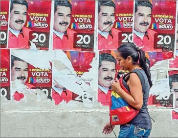  ?? JUAN BARRETO/AFP ?? A woman passes by posters of Venezuelan President Nicolas Maduro, in Caracas, on Saturday, on the eve of the country’s presidenti­al election.