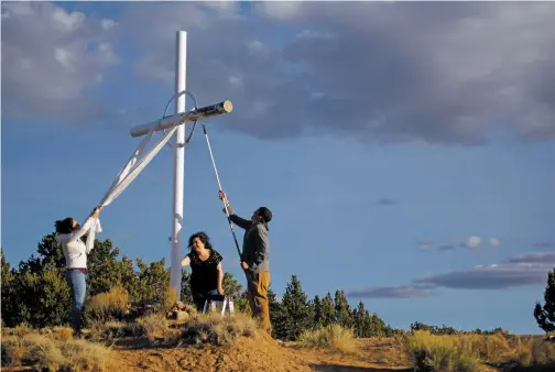  ??  ?? From left, Shantelle Quintana of Albuquerqu­e, Linda Medina of Las Vegas, N.M., and Nathan Leyba of Albuquerqu­e paint a cross near N.M. 503 on Thursday.