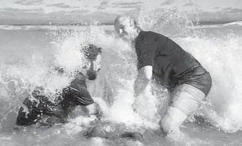  ?? ?? Paul Allen, a deacon, left, and the Rev. Jimmy Scroggins of Family Church perform a baptism last month in the Atlantic. Church members will often brace themselves against the waves and keep an eye out for sharks in an unusual setting for a religious rite.