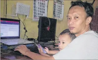  ?? INDAH NURUL HIDAYAH/ARIA KHRISNA VIA AP ?? Aria Khrisna and his 3-year-old son Raka at their home in Tegal, Indonesia. Khrisna, a 36-year-old father of three, says doing things like adding word tags to clothing pictures on websites such as ebay and Amazon pays him about $100 a month, roughly...