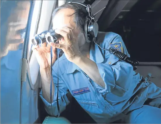  ??  ?? Vietnamese Air Force Col. Pham Minh Tuan uses binoculars on board an aircraft during a mission to search for the missing Malaysia Airlines flight MH370 in the Gulf of Thailand over the location where Chinese satellite images showed possible debris from...