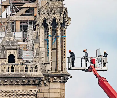  ??  ?? A team of repairmen is lowered by crane into the roof area to carefully remove mangled scaffoldin­g, some of which was melded to the weakened limestone walls in the fire