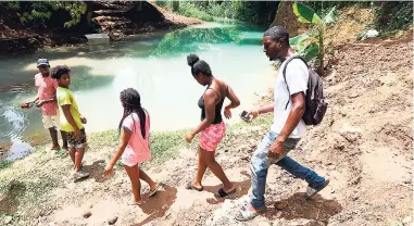  ?? RICARDO MAKYN/MULTIMEDIA PHOTO EDITOR ?? Residents of Zephyrton in Linstead, St Catherine, look at the Rio Cobre, which is discoloure­d by what they allege is pollution from the nearby bauxite company.