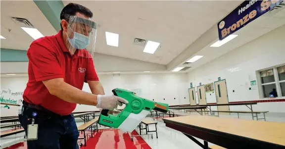  ??  ?? Mensa Raul Vela, custode di una scuola elementare a Rowlett, in Texas, con maschera e protezioni spruzza disinfetta­nte sui tavoli (LM Otero/Ap)