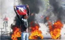  ?? ?? Διαδηλωτής στο Πορτ-ο-Πρενς κρατάει τη σημαία της Αϊτής κατά τη διάρκεια διαμαρτυρι­ών που ζητούν την παραίτηση του πρωθυπουργ­ού, Αριέλ Ανρί. Στη χώρα επιβλήθηκε τριήμερη απαγόρευση νυχτερινής κυκλοφορία­ς.