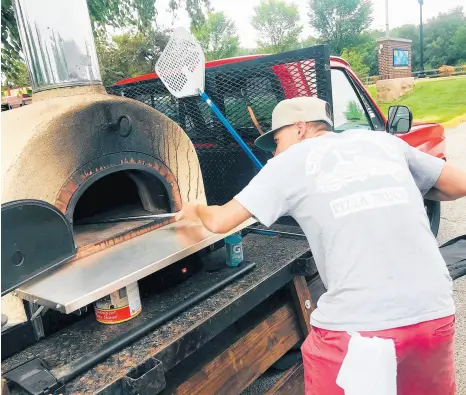  ?? JERRY DAVICH/POST-TRIBUNE ?? Brian Rock slides a hand-tossed gourmet pizza into his wood-fired oven Thursday at an outdoor summer market in Hobart.