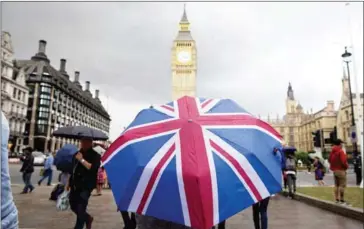  ?? AFP ?? A pedestrian shelters from the rain beneath a Union Jack umbrella near Big Ben at the Houses of Parliament in London on Saturday, following the pro-Brexit result of the UK’s EU referendum.