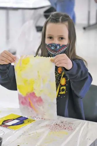  ??  ?? First-grade student, Annie, left, happily shows off a colorful piece of art she created during a morning workshop.